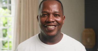 Afro-Amerikalı mutlu bir adamın portresi. Evdeki bir oturma odasında kameraya gülümsüyor. Otantik Aile Yaşam Tarzı, birlikte kaliteli zaman geçirmek. Aile Hayatı, Çeşitlilik, siyahi aile.