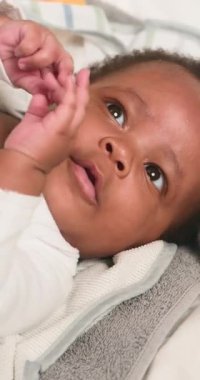 Sevimli Afrikalı Amerikalı bebek yumuşak bir battaniyeye uzanmış ellerini ve parmaklarını keşfediyor. Bebeklerin masum bakışları ve nazik hareketler çocukluk çağının gelişimi ve aile sevgisinin iç açıcı bir sahnesini yaratıyor..