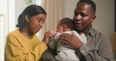 Sevgi dolu bir Siyah aile evde birlikte vakit geçirmekten zevk alır. Baba sevimli bebeğini tutarken, anne de çocukla nazikçe iletişim kuruyor. Sahne sıcaklığı, şefkati ve ebeveynliğin neşesini çağrıştırıyor..