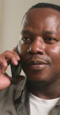 Bir adam evinde oturuyor ve cep telefonuyla hoş bir sohbet ediyor. Gülümsüyor ve ilgi çekiyor, açıkça bağlantının tadını çıkarıyor. Bu video mutluluk, rahatlama ve gündelik konuşmaları çağrıştırıyor..