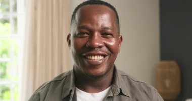 Mutlu bir Afrikalı Amerikalı adam evindeki kameraya gülümsüyor. Aile, babalık, mutluluk ve memnuniyet gibi kavramları temsil ediyor. Bu neşeli sahne sıcaklığı ve olumlu duyguları çağrıştırıyor. Reklam kampanyaları için ideal..