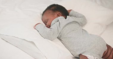 Şirin bir Afrikalı Amerikalı bebek rahat beyaz bir yatakta mışıl mışıl uyuyor, tatlı rüyalar görüyor. Huzurlu atmosfer rahatlama ve sükuneti teşvik eder, rahatlık ve sıcaklık hissi yaratır..