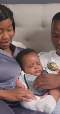 Mutlu bir aile yatakta birlikte oturur. Ebeveynler bebeklerini sevgiyle kucaklar, o da çıngırakla oynar ve esner. Sessiz bir aile bağının tadını çıkarıyorlar..