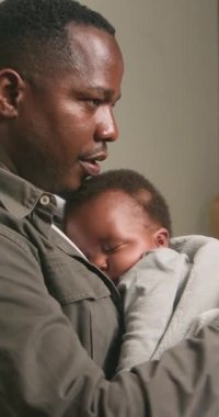 Sevgi dolu bir baba, uyuyan bebeğini nazikçe göğsüne yakın tutar. Bebek yumuşak bir battaniyeye sarılmış ve babasının kollarında huzur içinde yatıyor. O hassas an, ebeveynler ve çocuklar arasındaki bağı yakalar..