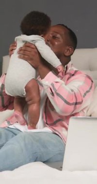 Mutlu bir baba, evde çalışırken sevimli bebeğiyle vakit geçirmekten zevk alır. Bebeğini kaldırır ve onunla oynar. Yürek ısıtan bir aile, aşk ve iş hayatı dengesi sahnesi yaratır. Bebek sağlıklı ve mutlu görünüyor..