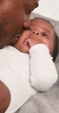 Sevgi dolu bir baba, sevimli bebeğine gülümser. Yumuşak bir battaniyenin üzerine uzanır ve parmaklarını emer. Bebek geniş gözlerle babalarına bakıyor. Bu iç açıcı sahne ebeveyn ve çocuk arasındaki hassas bağı yakalar..