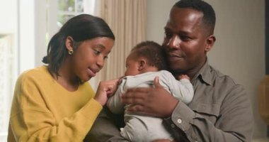 Genç siyahi bir aile evde birlikte vakit geçirmenin keyfini çıkarıyor. Baba bebeğini kucağında tutarken anne neşeyle etkileşime girer. Sıcak, sevgi dolu ve samimi bir ortam yaratırlar. Bu sahne aile bağlarının ve aile sevgisinin özünü yansıtıyor..