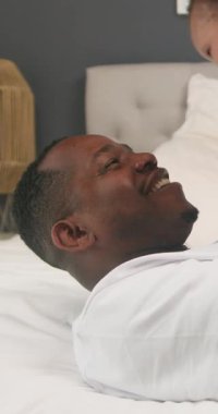 Mutlu bir Afrikalı Amerikalı baba yatakta yatar ve bebeğini havaya kaldırır. Bebek beyaz tulum giyer ve baba beyaz gömlek giyer. Birbirlerine gülümsüyorlar ve ailecek vakit geçiriyorlar..