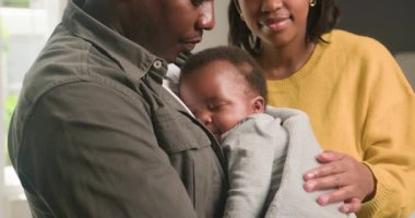 Sevgi dolu bir Siyah aile, evlerinde hassas bir anı paylaşıyor. Baba, uyuyan bebeğini yanında tutarken, anne de ufaklığı nazikçe sakinleştiriyor. Sahne sıcaklığı, güvenliği ve ebeveynliğin neşesini anımsatıyor..