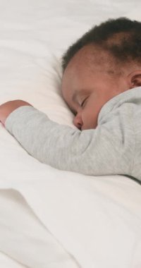 Tatlı bir Afrikalı Amerikalı bebek yumuşak, beyaz bir yatakta mışıl mışıl uyuyor, tatlı rüyalar görüyor. Bebek rahat gri pijamalar giyiyor. Bu huzurlu görüntüler huzur, sükunet ve çocukluğun basit zevklerini çağrıştırıyor..