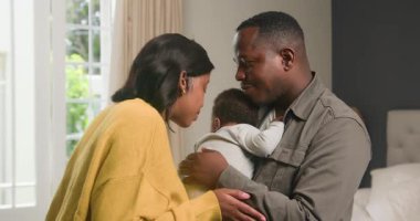 Sevgi dolu bir siyahi aile yatak odasında hassas bir anı paylaşır. Anne çocuğun başını nazikçe öperken baba uyuyan bebeğini tutar. Bu iç açıcı sahne aile bağlarının ve aile sevgisinin özünü yansıtıyor..