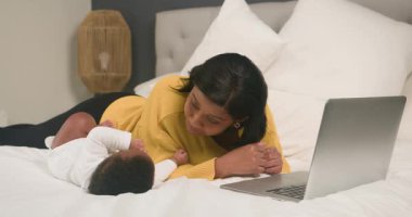 Bir anne bebeğiyle yatakta yatar ve dizüstü bilgisayarı üzerinde çalışır. Bebeğiyle konuşurken, yeni doğmuş bir bebekle evde çalışmanın zorluklarını anlatıyor. Bu iç açıcı sahne, çalışan bir annenin sevgisini ve adanmışlığını yansıtıyor..