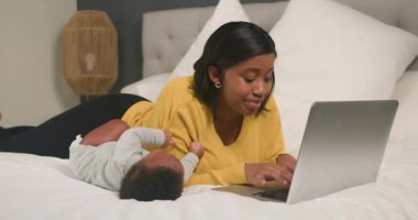 Genç bir anne sevecen bir şekilde birden fazla iş yapar. Sevimli bebeği rahat yatağında yatarken dizüstü bilgisayarı üzerinde çalışır. İş ve anneliği nazik bir gülümsemeyle dengeliyor. Modern aile hayatının iç açıcı bir sahnesini oluşturuyor..