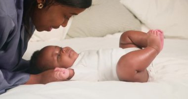 Sevgi dolu bir Afrikalı Amerikalı anne gülümser ve beyaz bir yatakta uzanmış sevimli bebeğini öper. Bebek küçük bacaklarını ve ayaklarını şakacı bir şekilde tekmelerken annesine bakar. Sahne, sevgi, sıcaklık ve aile bağlarını çağrıştırıyor..