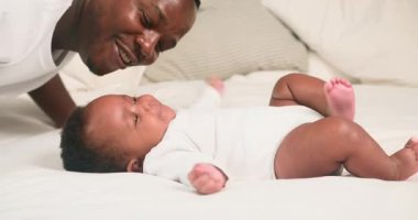 Sevgi dolu bir baba, sevimli bebeğiyle rahat bir yatakta oynar. Beyaz tulum giyen bebek, babasının gülümsemesi ve bebek yüzünü öpmesi gibi şakacı bir şekilde ayaklarını çırpar. Sahne sıcaklığı, sevgiyi ve aile bağını çağrıştırıyor..