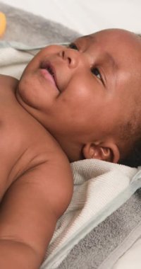 Yumuşak, gri ve krem kapüşonlu havluya sarılı mutlu, tombul bir erkek bebek gülümseyip etrafa bakıyor. Bebek ürünleri, aile anları, çocuk bakımı ve yeni doğan kavramları için mükemmel. Bu video, bebekliğin saf neşe ve masumiyetini yansıtıyor..