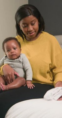 Sevgi dolu bir Afrikalı Amerikalı anne, sevimli bebeğiyle bir yatakta oturuyor. Çocuğuyla nazikçe etkileşime girer ve yanındaki beyaz çarşafı düzleştirir. Evde şefkatli ve iç açıcı bir an yaratır..