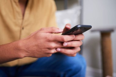 Kapalı mekanda el ele tutuşup akıllı telefon kullanmak. Sahne, rahat ve sessiz bir ev ortamında dijital etkileşimin, muhtemelen gezinmenin ya da mesajlaşmanın gündelik ve samimi bir anını gösteriyor..