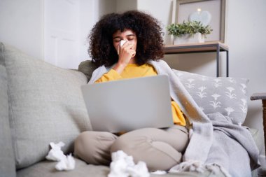 Sıcak bir oturma odasında bir kadın soğuk algınlığıyla uğraşırken dizüstü bilgisayarını kullanır. O bir mendil tutuyor, bir battaniyeye sarılı ve buruşuk mendillerle çevrili. Sahne dinlenme ve kendine bakımı gösteriyor..