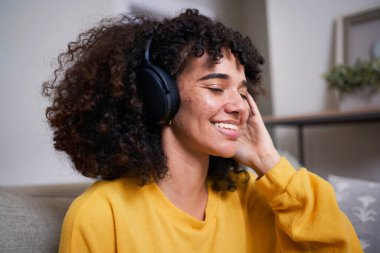 Kulaklık takan neşeli bir kadın evinde müziğin keyfini çıkarırken gülümsüyor. Onun gevşek ifadesi ve gelişigüzel ayarları bir neşe ve rahatlama duygusunu yansıtıyor..
