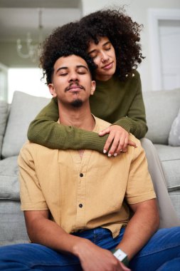 Neşeli bir çift sıcak bir yaşam alanında yerde otururken sevgi dolu bir şekilde kucaklaşır. Keyifli ve huzurlu görünüyorlar, rahat bir ev ortamında bir anlık yakınlık ve sıcaklığın tadını çıkarıyorlar..