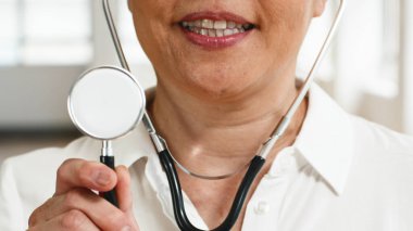 Stetoskop tutarken içten gülümseyen, tıp alanında güven ve uzmanlığı sembolize eden ilgili bir sağlık uzmanının yakın plan resmi. Sağlık ve refahla ilgili kavramlar için ideal.