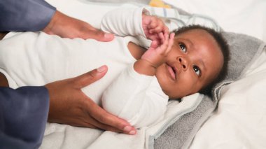 Bebek bezi değiştirirken bir bakıcının nazikçe bir bebekle ilgilendiğini gösteren dokunaklı bir görüntü. Sahnede bakım, güven ve bir bakıcı ile rahat bir yuva ortamında bir çocuk arasındaki bağ vurgulanıyor..