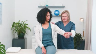 Yetenekli bir kıdemli fizyoterapistin genç siyahi müşterilere omuz ve kol tedavisi uygulamasını izleyin. Bu sahnede profesyonel spor fizyoterapisi ve rehabilitasyon hizmetleri 