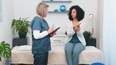 Üst düzey bir fizyoterapist, genç bir siyahi müşterinin profesyonel muayene sırasında bilek ağrısı hakkındaki endişelerini özenle dile getirirken,. 