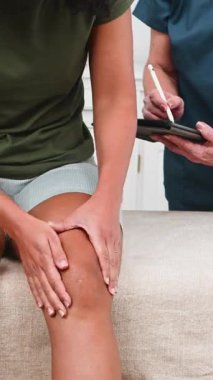 Üst düzey bir fizyoterapist ayrıntıları dikkatle not ederken siyah bir müşteri fiziksel terapi seansı sırasında diz ağrısını tarif ediyor. Bu, etkili rehabilitasyon, profesyonel bakım ve hastaların iyileşmesini temsil eder..