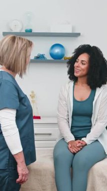 Deneyimli bir kadın fizyoterapist modern bir sağlık kliniğinde gülümseyen genç bir siyahi müşteriye danışmanlık yapıyor. Sağlık, rehabilitasyon ve iyileşme ve kişiselleştirilmiş tedavi planlarını tartışırlar..