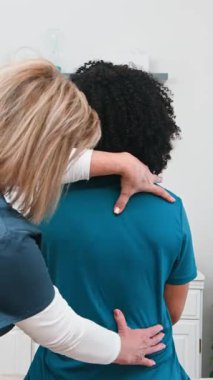 Yetenekli bir kıdemli fizyoterapist, siyah bir kadın müşterinin omuzlarını ve sırtını elleriyle tedavi eder. Bu profesyonel seansta klinik ortamda rehabilitasyon ve ağrı kesiciler üzerinde duruluyor..