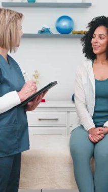 Üst düzey bir fizyoterapist rehabilitasyon sırasında genç bir siyahi kadın müşteriye ustaca danışıyor. Aktif olarak dinliyor ve not alıyor. Kişiselleştirilmiş fizik tedavi planı için hastaların spor yaralarını değerlendiriyor..