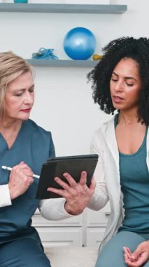 Üst düzey bir fizyoterapist genç siyahi müşterisiyle dijital tablet kullanarak kişiselleştirilmiş tedavi planını ustaca tartışıyor. Bu, profesyonel sağlık hizmetleri, modern terapi ve bir klinik ortamında hasta ilişkileri vurguluyor.