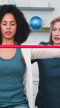 Üst düzey bir fizyoterapist genç siyahi müşterisine fizik tedavi seansında direniş bandı egzersizinde rehberlik eder. Bu kendini spora adamış fizyoterapist rehabilitasyon, güç, sağlık ve sağlıklı bir iyileşme için uzman bakımı sunuyor..