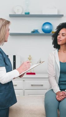 Deneyimli bir kıdemli fizyoterapist, parlak, modern bir rehabilitasyon kliniğinde muayene sırasında çektiği acı ve semptomları anlatan genç Siyahi kadın müşterisini dikkatle dinler..