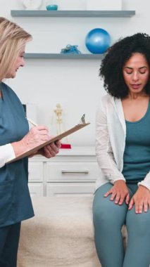 Üst düzey bir fizyoterapist parlak ve modern bir klinikte genç bir siyahi kadın müşteriyle görüşürken dikkatle not alır. Bu profesyonel etkileşim fiziksel terapi seansı sırasında sağlık, sağlık ve kişisel bakıma odaklanır..