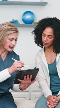 Tecrübeli bir fizyoterapist, deneyimli bir spor fizyoterapisti, özenli genç siyahi müşterisine kişisel rehabilitasyon programını açıklamak için bir tablet kullanıyor. İyileşme ve iyileşme sürecini tartışıyorlar..