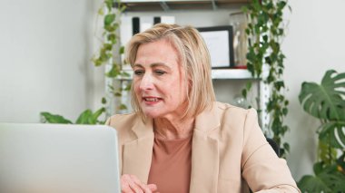 Yeşil bitkilerle profesyonel bir ofiste çalışan resmi giyinmiş yaşlı bir kadın..