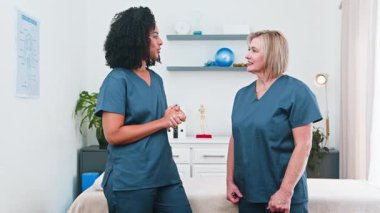 İki farklı kadın fizyoterapist, modern kliniklerinde beşlik çakarak bir başarı ve pozitif işbirliği anını paylaşıyor. Bu, gelişmekte olan küçük işletme ve spor bilimi ortamındaki profesyonel danışmanlığı vurguluyor.