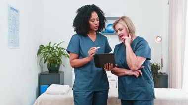 Hasta bakımı konusunda işbirliği yapan iki farklı kadın fizyoterapist modern kliniklerindeki bir tabletin dijital kayıtlarını inceliyor. Başarılı küçük işletme uygulamalarında etkili takım çalışması ve akıl hocalığı gösterirler..