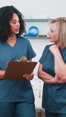 Tıbbi önlük giyen iki farklı kadın fizyoterapist modern bir klinik ortamında spor bilimi ve hasta bakımı üzerine odaklanmış bir tartışmaya girişiyor. Uzman sağlık hizmetleri tavsiyesi ve rehabilitasyon sağlamak için işbirliği yapıyorlar.