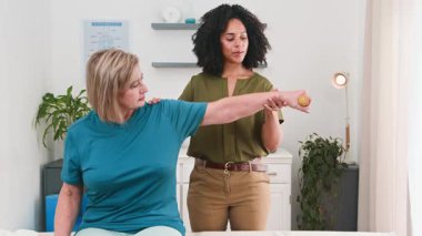 Yetenekli bir siyahi kadın biyokinetik uzmanı kıdemli bir hastaya rehabilitasyon kolu egzersizleri yaptırarak profesyonel fizyoterapi bakımı ve iyileşme ve hareketlilik desteği sunuyor..