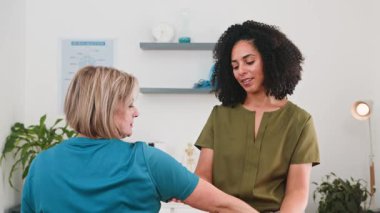 Siyahi bir kadın olan uzman biyokinetik uzmanı, kol rehabilitasyonu ve hareket üzerine yoğunlaşarak kıdemli bir hastaya kendini adamış bir fizyoterapi uyguluyor. İşbirlikçi toplantıları bir klinikte sağlık ve iyileşmeyi teşvik eder..