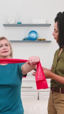 Kendini adamış siyah bir biyokinetik uzmanı etkili direniş bandı egzersizlerinde kıdemli bir hastaya rehberlik ediyor. Bu odaklanmış fizyoterapi seansı, daha sağlıklı bir yaşam tarzının geliştirilmesi, hareket kabiliyeti ve genel fiziksel refahı hedeflemektedir..