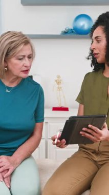 Profesyonel bir siyahi kadın fizyoterapist ya da biyokinetik uzmanı, uzman bir hastayla tedavi seçeneklerini ve spor bilimi anlayışlarını dikkatlice tartışır. Dijital tablette sağlık süreci ve rehabilitasyon planlarını birlikte gözden geçirirler..