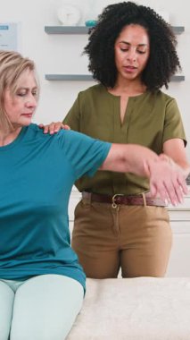 Deneyimli siyahi kadın fizyoterapist, omuz ve kol hareketleri egzersizleri yapan, fiziksel rehabilitasyon ve hareket kabiliyetinin geliştirilmesine odaklanan yaşlı bir hastaya yardım ediyor. Bu oturum profesyonel sağlık hizmetleri ve kişiselleştirilmiş terapiyi vurguluyor.