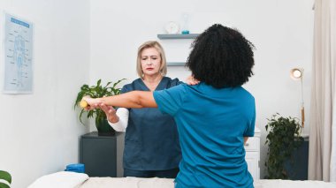 Kıdemli bir fizyoterapist, gülümseyen siyah bir müşterinin kolunda spor masajı ve fizik tedavi seansını ustalıkla gerçekleştirir. Temiz, modern küçük uygulama, kişiselleştirilmiş sağlık, iyileşme ve genel refahın altını çizmek