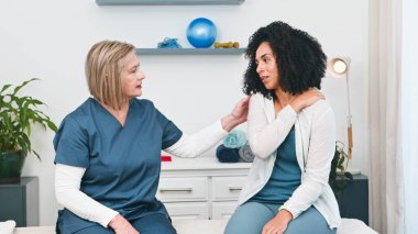 Deneyimli bir kıdemli fizyoterapist, küçük ve modern kliniğinde omuz ağrısı çeken genç bir siyahi müşteriye şefkat gösteriyor. Hasta-terapist iletişimi, güven ve yaraların iyileşme ve iyileşme süreci.