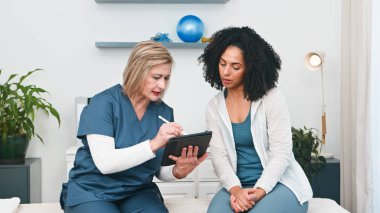 Deneyimli bir kıdemli fizyoterapist genç bir siyahi müşteriye kişisel spor fizyoterapi danışmanlığı sağlar. Dijital tablet üzerindeki önemli bilgileri gözden geçirirler, tedavi planları ve spor masajı ve iyileşme süreci hakkında tartışırlar.